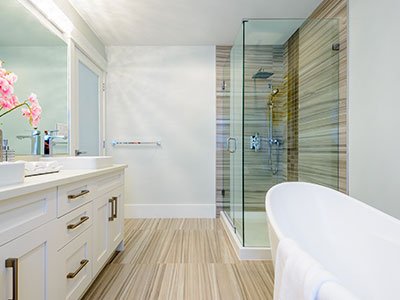 Average bathroom with light gray walls, brown striped tiles on the floor and shower wall, white cabinets, white bathtub, and large mirror.
