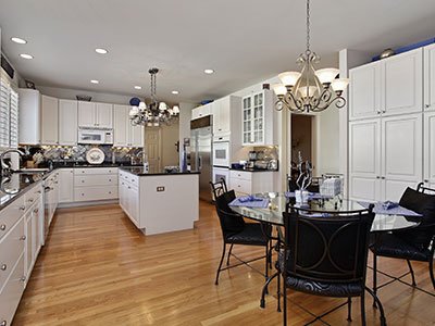 Large kitchen with white cabinets, round glass table, black chairs, wooden floor, and two chandeliers.