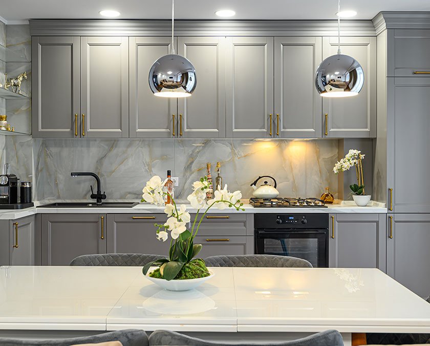 Large luxury kitchen with gray cabients and overhang lighting and whit emarble countertops