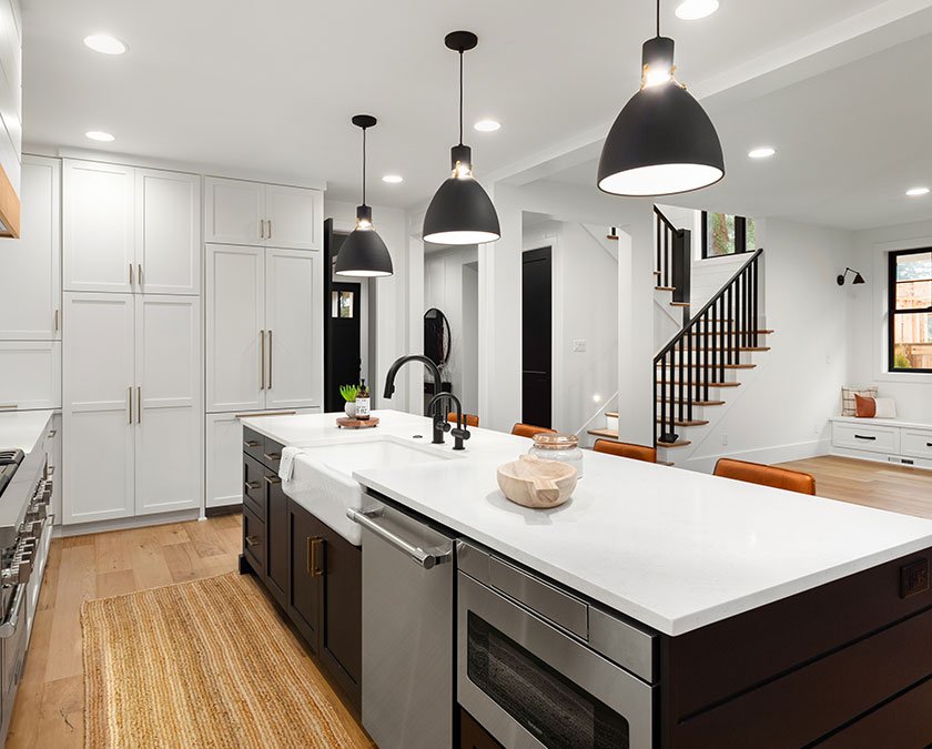 Modern kitchen with white cabinets, large dark island with white countertop, modern lighting, and wooden floor.