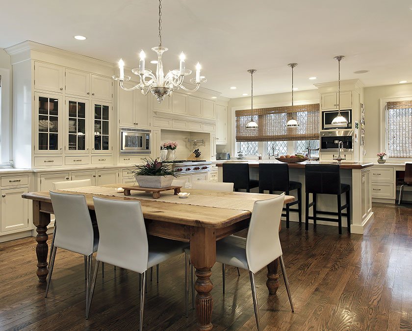 Modern kitchen with white cabinets, wooden table, white chairs, elegant chandelier, and wooden floor.