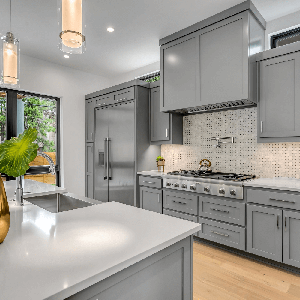Modern kitchen with white cabinets, silver finish appliances, modern lighting, large island with white countertop, and wooden floor.